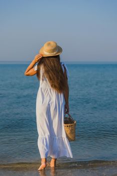 woman in a hat and with a basket in her hands is walking on the beach