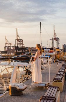 a girl in a white dress stands on the pier against the background of the sea