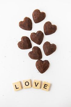 Truffle chocolate candies in the form of a heart on a white background. Inscription love made of wood letters