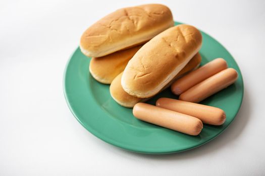 Fresh hot dog buns which lie on a green plate along with sausages. Top view, close-up