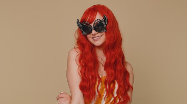 Portrait of seductive cheerful stylish redhead woman in tank top wearing sunglasses, charming smile. People happy emotions. Young lovely ginger girl posing isolated alone on beige studio background