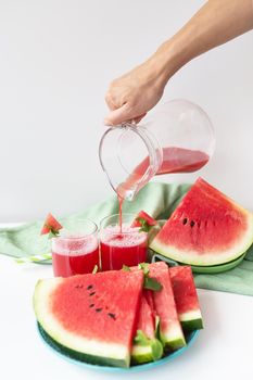 The girl pours from a jug freshly squeezed juice from fresh watermelon, a healthy smoothie from watermelon and mint leaves