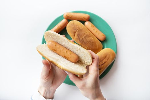 Fresh buns for making hot dogs that lie on a green plate along with sausages that the girl holds in her hands. Top view, close-up