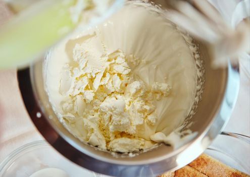 Top view of mascarpone cheese in bowl of food processor with whipped cream. Mixing, whipping cream for traditional Italian dessert Tiramisu cake. Step by step recipe. Homemade food, culinary concept.