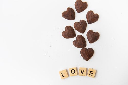 Truffle chocolate candies in the form of a heart on a white background. Inscription love made of wood letters. Place for an inscription