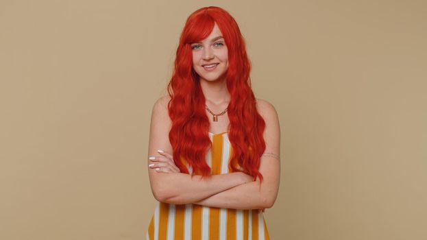 Cheerful lovely redhead adult woman in striped tank top smiling and looking at camera. Young fashion model girl with gray eyes indoors studio shot isolated on beige background. Female nature beauty