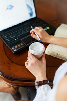 Young woman working on a laptop at home at the table, online learning on PC, e-learning. Work online, remote work. Close-up view over the shoulder