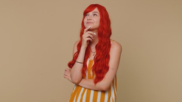 Redhead young woman in thought and conjectures looking to side, dreaming, imagining something pleasant, fantasizing about weekends holidays. Red hair ginger girl isolated on beige studio background
