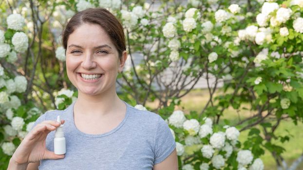 Happy woman demonstrating nasal spray on the background of a blossoming tree