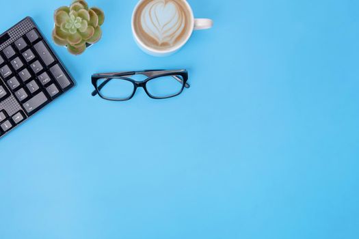 Black keyboard, coffee, glasses, plant on blue background. workplace. Space for text. The financial checks
