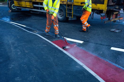 Road workers applying hot red road marking paint on new build road