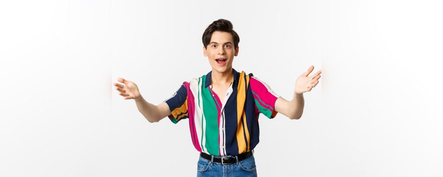 Amazed young handsome man reaching hands forward, want to hold or take something, looking with desire, standing over white background.