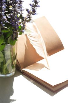 Still life with open book and quill pen near posy of wildflowers