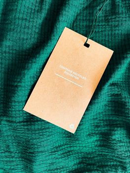 Contains recycled polyester fashion label tag, sale price card on luxury emerald green fabric background, shopping and retail concept