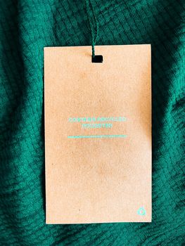 Contains recycled polyester fashion label tag, sale price card on luxury emerald green fabric background, shopping and retail concept