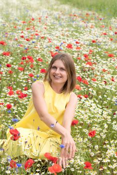 a beautiful young blonde woman in a yellow dress stands among a flowering field of poppies, daisies, cornflowers and laughs. High quality photo