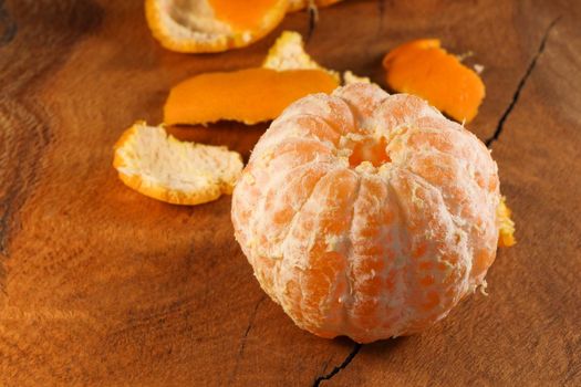 Fully peeled fresh satsuma mandarin tangerine (Citrus unshiu) citrus fruit on natural wood surface