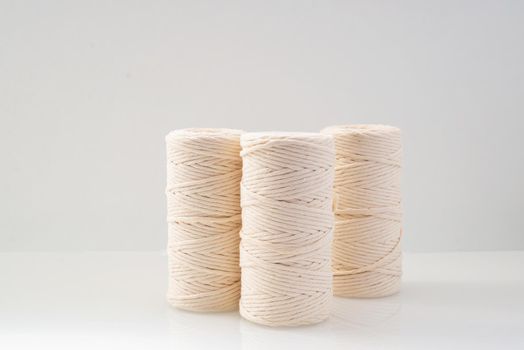 macrame threads wound bobbins of natural beige color are located on a light background