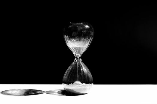 Hourglass, sandglass with sand on a black background with a streak of white light and a shadow