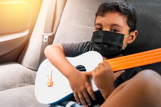Latin boy in the back seat of a car with a ukulele in his hands