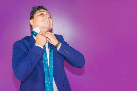 Latin Nicaraguan man in a blue suit having trouble tying his tie knot on a flat purple background