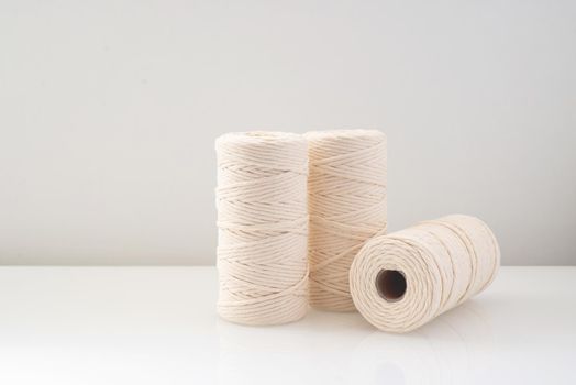 macrame threads wound bobbins of natural beige color are located on a light background
