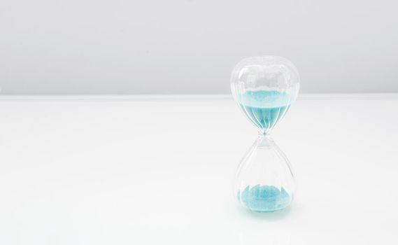Hourglass on bright light, sandglass with blue sand on white background