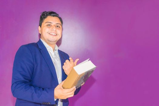 Latin Nicaraguan university professor in blue suit on flat purple background pointing a book