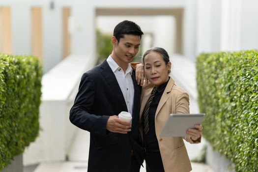 Portrait of Asian Senior Business woman and young business man discussing about project by digital tablet. Account and Finance concept