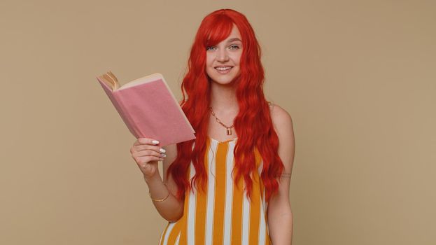 Redhead young woman reading funny interesting fairytale story book, leisure hobby, knowledge wisdom, education learning, study, wow. Red hair ginger girl isolated alone on beige studio wall background