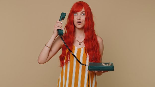 Hey you, call me back. Cheerful one ginger woman secretary in tank top talking on wired vintage telephone of 80s, says hey you call me back. Young redhead girl posing isolated on beige wall background