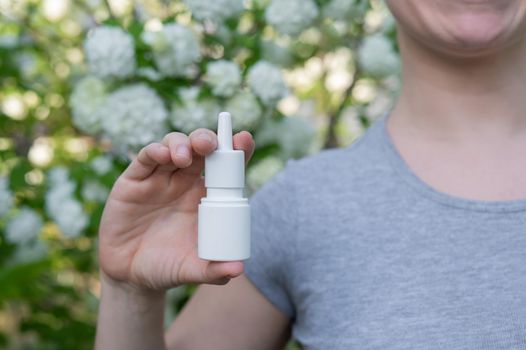 Happy woman demonstrating nasal spray on the background of a blossoming tree