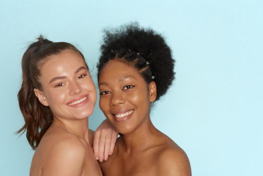Caucasian and african american women with perfect skin on blue background with copy space. Skin care, hair care, moisturizing, cosmetology and spa