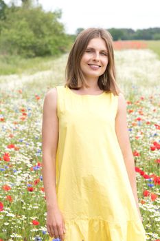 a beautiful young blonde woman in a yellow dress stands among a flowering field of poppies, daisies, cornflowers and laughs. High quality photo