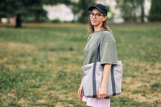 Young woman with glasses holding empty cotton eco bag, mockup design. High quality photo