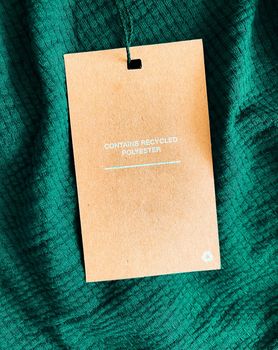 Contains recycled polyester fashion label tag, sale price card on luxury emerald green fabric background, shopping and retail concept