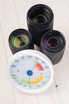 white analog Thermometer and Hygrometer with photography equipments. Lenses and camera equipment are optimally stored at a relative humidity (RH) of around 35% to 45%.