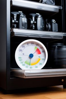 white analog Thermometer and Hygrometer with photography equipments. Lenses and camera equipment are optimally stored at a relative humidity (RH) of around 35% to 45%.
