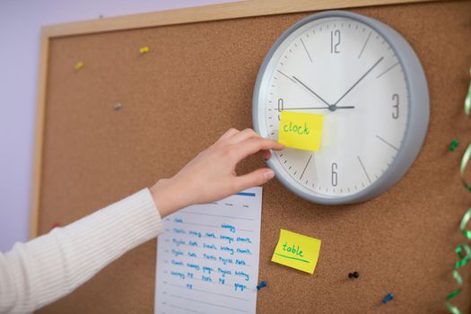 A large wall clock on which is glued a yellow card with the word in English - clock. Individual learning of a foreign language at home.