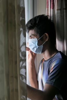 A young man with protective mask looking through window .