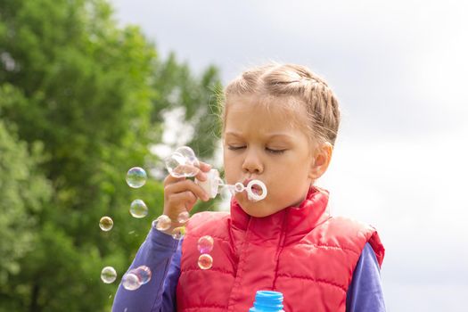 Caucasian little girl of 6 years blowing bubbles in summertime