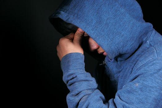 sad man in hood cover face with hands isolated in black