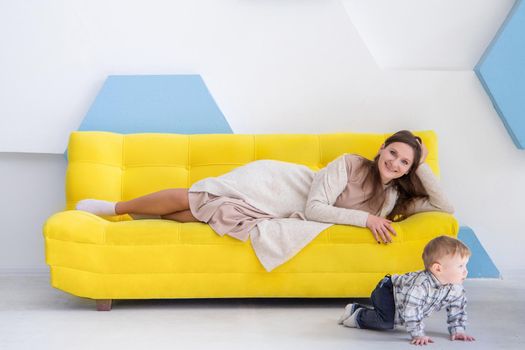 Portrait of a young european woman with a small child on a sofa in a bright positive interior.