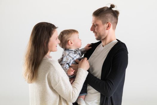 Young parents hold their child in their arms and look at him on a white background.