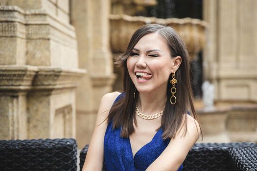 Funny pretty smiling with tongue woman in blue dress outdoor emotional portrait.