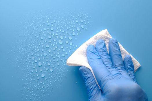 hand in blue rubber gloves cleaning table with towel .