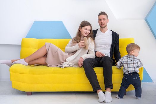 Studio shot of a young family of 3 on a yellow sofa.