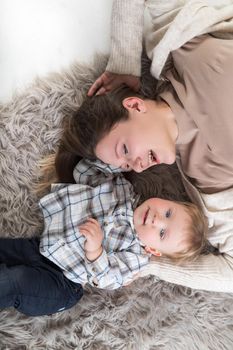 A young mother with her child lie on a cozy rug and have fun together. Top view.