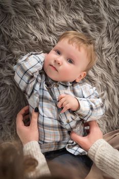 Portrait of a serious one-year-old kid who is lying on a cozy rug with which his mother spends time. Top view.