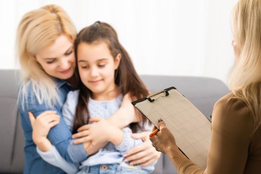 Hand of a professional family psychotherapist writing notes in front of a family with a child during a consultation.